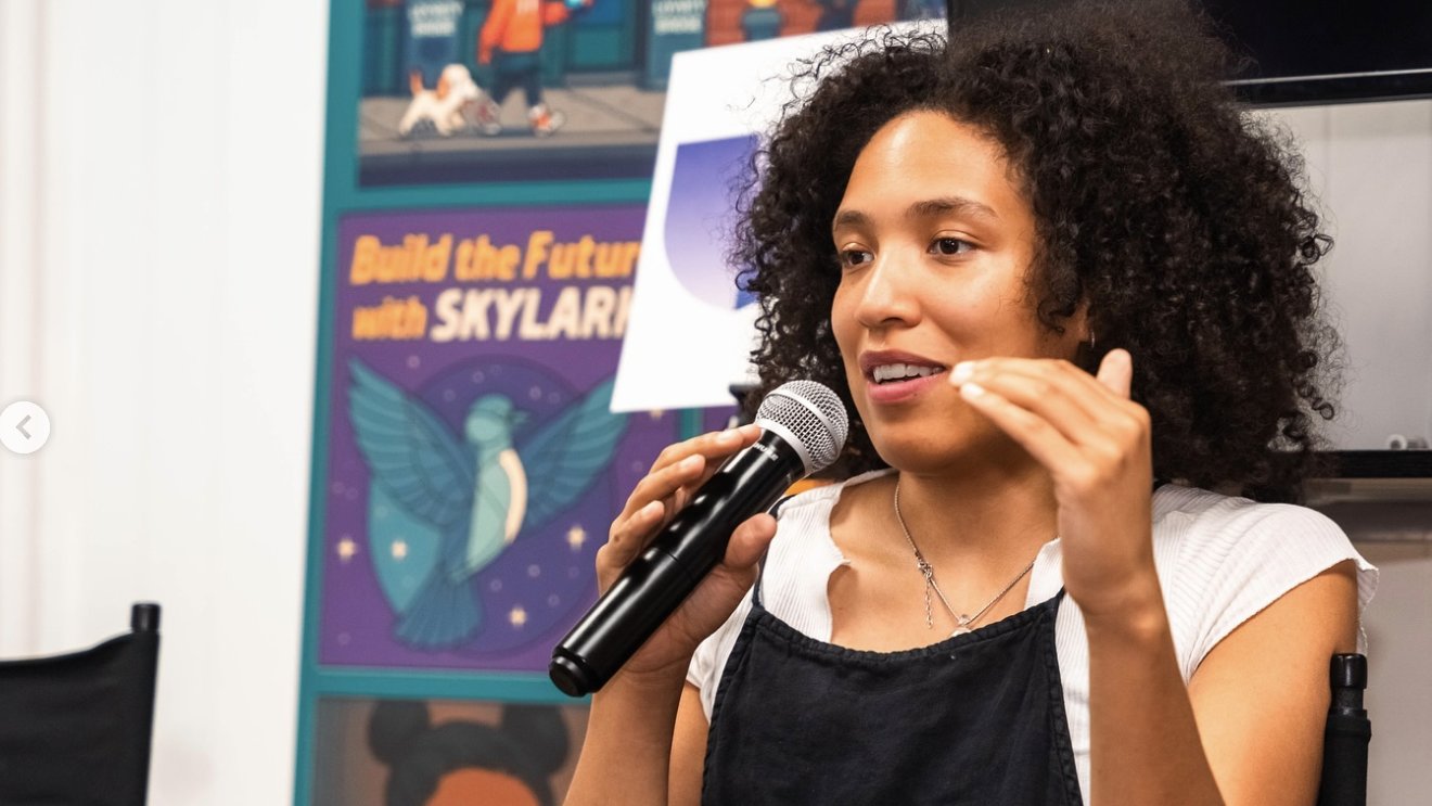 Laila Jhané speaking with a microphone at the Decentralized Intelligence talk, Atlanta Blockchain Center.