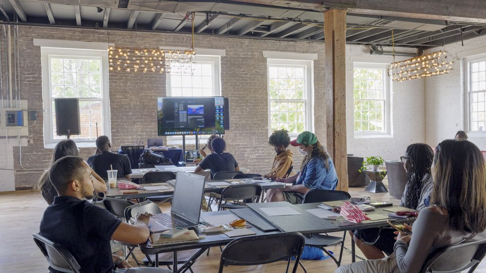 Participants working at laptops during the Pepper's Ghost workshop at The Goat Farm, daylight through the factory windows.